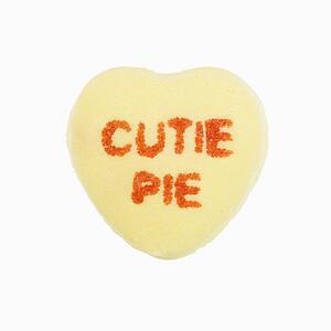 Yellow candy heart that reads cutie pie against white background.