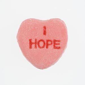 Pink candy heart that reads I hope against white background.