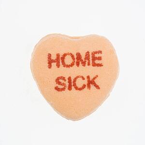 Orange candy heart that reads home sick against white background.