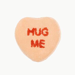 Orange candy heart that reads hug me against white background.