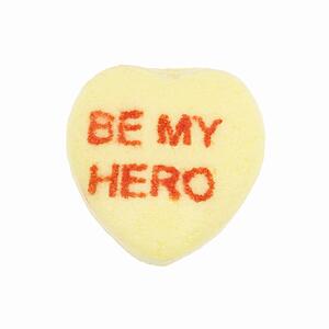Yellow candy heart that reads be my hero against white background.