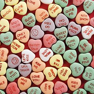 Large group of colorful candy hearts with sayings on them arranged on red background.