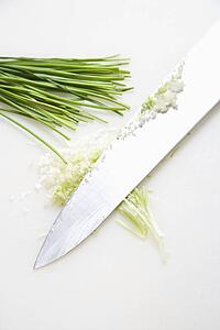 Freshly chopped chives with kitchen knife resting on countertop.