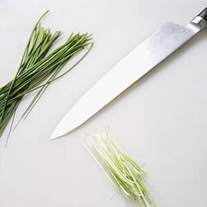 Fresh chives with kitchen knife resting on countertop.