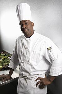 African-American male chef wearing traditional uniform and toque looking at viewer.
