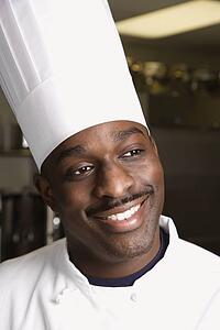 Head shot of smiling African-American male chef wearing traditional uniform and toque.
