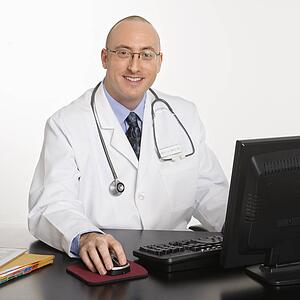 Caucasian mid adult male physician sitting at desk with laptop computer.