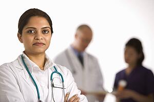 Indian mid adult woman doctor standing with medical staff in background.