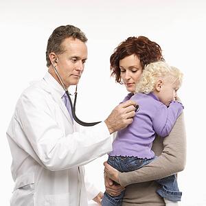 Middle-aged adult Caucasian male doctor holding stethoscope to female toddler's back with mother watching.