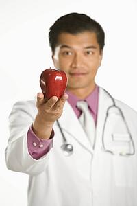 Asian American male doctor holding out apple.