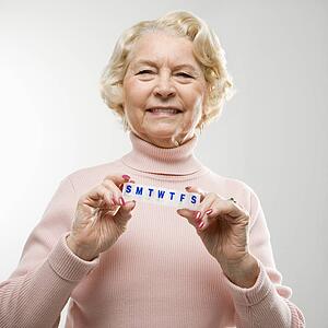 Caucasian senior woman holding pill box and smiling at viewer.