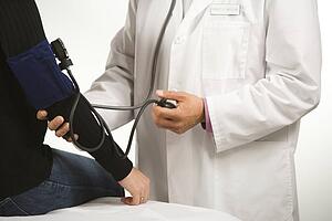 Asian American male doctor testing blood pressure of Caucasian woman.