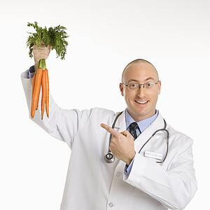 Caucasian mid adult male physician holding and pointing to bunch of carrots.
