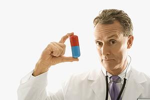 Mid-adult Caucasian male doctor holding an oversized medical pill.