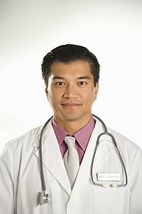 Portrait of Asian American male doctor against white background.