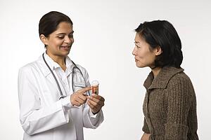 Indian woman doctor explaining medication to Asian woman patient.