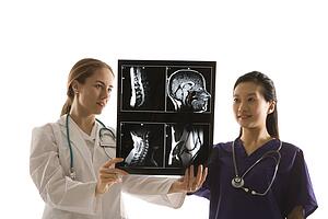 Caucasian and Asian Chinese mid-adult female doctors analyzing x-ray. 