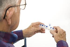 Profile view of Caucasion elderly man holding seven-day pill box with Thursday open.
