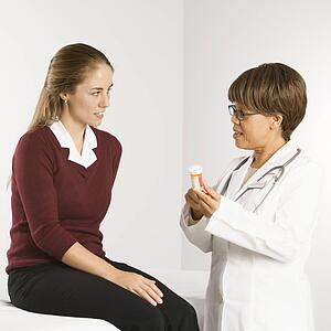 African American middle-aged female doctor explaining medication to Caucasian mid-adult female patient.