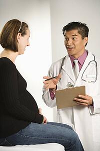 Asian American male doctor examining Caucasian pregnant female patient.