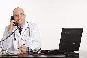 Caucasian mid adult male physician sitting at desk with laptop computer.