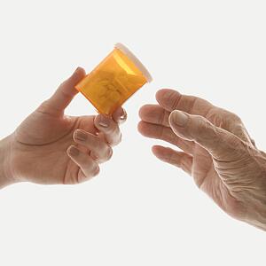 Close-up of mid-adult Caucasian female's hand handing medication bottle to elderly Caucasian male hand.