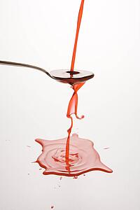 Stream of red cough syrup overflowing spoon into puddle below.