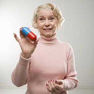 Caucasian senior woman holding oversized pill at viewer.