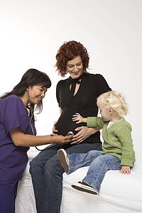 Nurse holding stethoscope on Caucasian pregnant woman's belly.