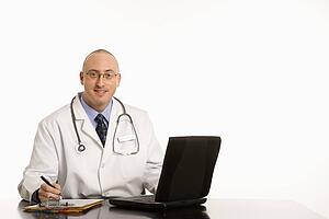 Caucasian mid adult male physician sitting at desk with laptop computer.