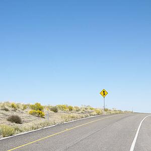 Road disappearing into horizon with merge road sign.