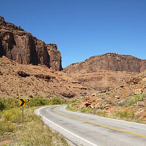 Road curving to right with red rock cliffs in Utah.