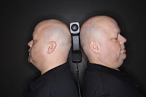 Identical twin men standing back to back with telephone balancing between them.