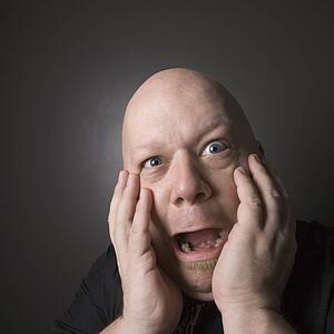 Bald man with hands to face making scared facial expression