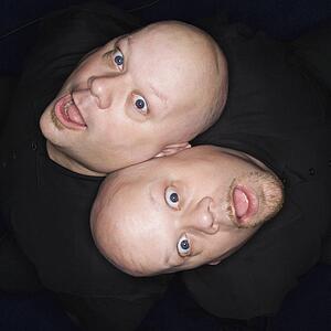 Aerial view of bald identical twin men sitting back to back making facial expressions.