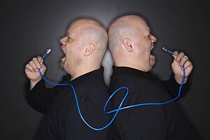 Bald mid adult identical twin men standing back to back yelling into ethernet cable.