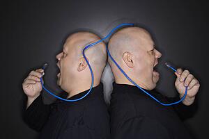 Bald identical twin men standing back to back yelling into ethernet cable