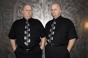Bald mid adult identical twin standing together looking at viewer.