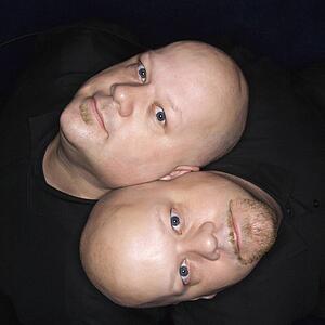 Aerial view of bald identical twin men sitting back to back and looking up at viewer