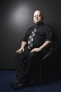 Mid adult bald man wearing necktie sitting and looking at viewer.