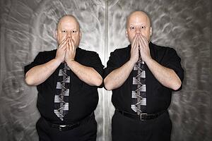 Bald mid adult identical twin men gasping with hands over mouth.