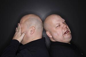 Bald identical twin men standing back to back with sad expressions