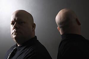 Mid adult bald identical twin men standing back to back and looking at viewer.