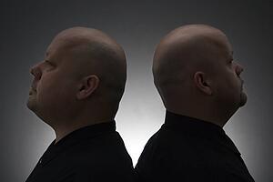 Mid adult bald identical twin men standing back to back.