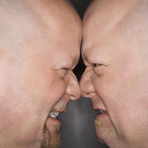 Close up of bald mid adult identical twin men standing face to face with angry expression.