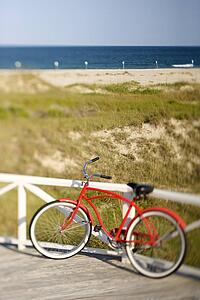 Red beach cruiser bicycle leaning against walkway rail on beach on Bald Head Island, North Carolina.
