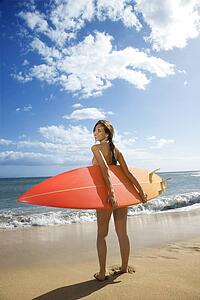 Young pretty woman in bikini standing with surfboard at beach 