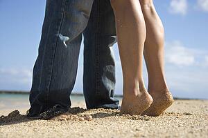Feet and legs of mid-adult Caucasian couple standing together on beach. 