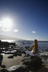 Young adult Asian Filipino female meditating on rocky beach 