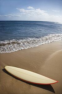 Surfboard on sandy beach with ocean in background 